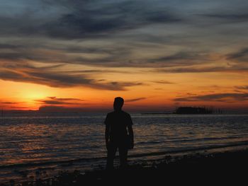 Silhouette man with hand raised standing at beach against sky during sunset