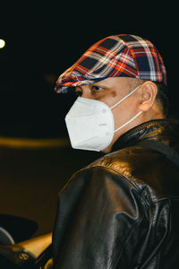 Close-up side view portrait of a masked man sitting on a motorcycle on the street at night 