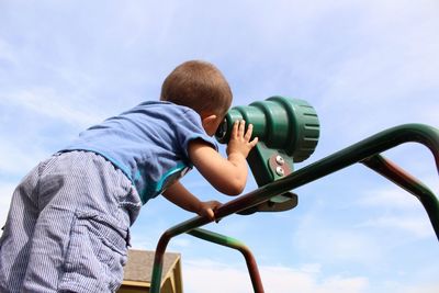 Low angle view of boy looking through hand-held telescope against sky