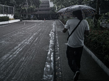 Rear view of man walking on wet road in rainy season