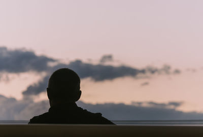 Rear view of silhouette boy against sea at sunset