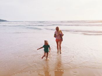 Full length of mother and daughter walking on shore at beach