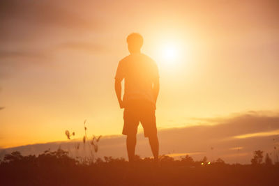 Rear view of silhouette man standing on field against sky during sunset