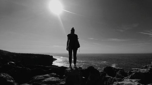 Silhouette man standing on rock by sea against clear sky