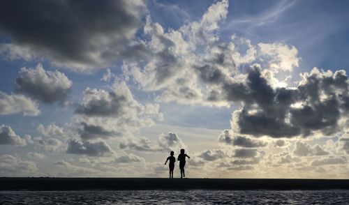 Silhouette people walking at beach against sky