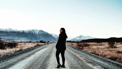 Rear view of woman standing on road towards mountains against sky