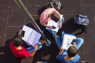 High angle view of friends using mobile phones while studying on footpath during sunny day