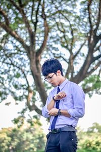 Young man adjusting sleeve while standing against trees