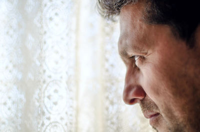 Close-up of thoughtful man looking away by curtain