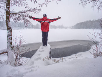 Man in red dark clothes standing on the winter snowy bank of the unfrozen river