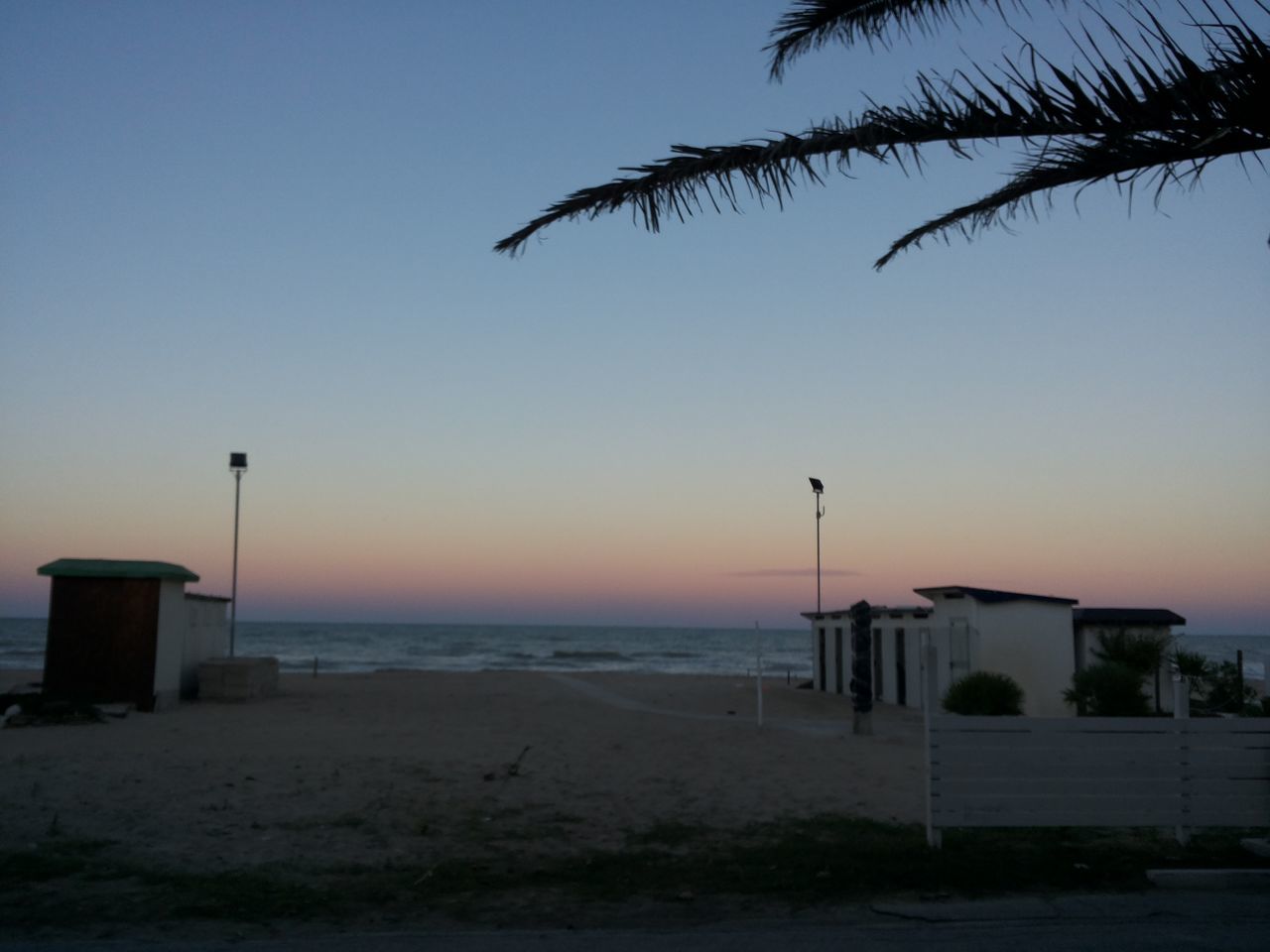 sea, sunset, beach, clear sky, horizon over water, tranquility, shore, orange color, copy space, tranquil scene, scenics, nature, sand, sky, built structure, water, street light, beauty in nature, outdoors, tree