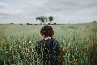 Rear view of girl standing by plants against sky