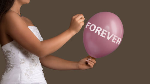 Midsection of bride holding balloon and needle against gray background