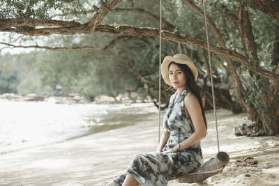 Portrait of young woman sitting on swing at beach