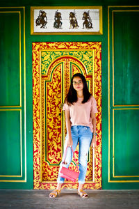 Portrait of young woman standing against door