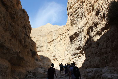 Rear view of people hiking amidst rocky mountains at wadi og