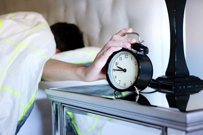 Close-up of man touching alarm clock while sleeping on bed at home