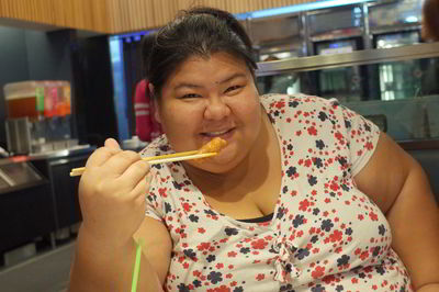 Portrait of happy overweight woman eating with chopsticks at restaurant