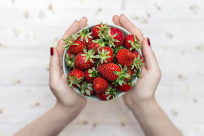 Cropped hands holding strawberries in bowl at table