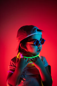 Cyberpunk boy child in white t shirt and sunglasses neon sticks on neck listening music on wall