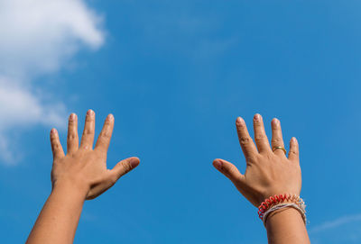 Cropped hands of people against blue sky