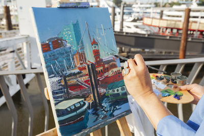 Hand of artist painting on easel at harbor