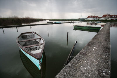 Rowboats moored in harbor against cloudy sky