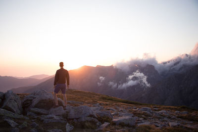 Rear view of man standing on mountain against sky during sunset