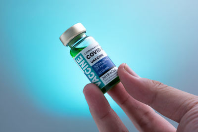 Close-up of hand holding bottle against blue background