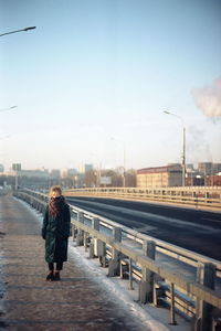 Man standing on railing in city against sky