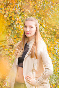 Portrait of young beautiful woman standing by autumn tree branches