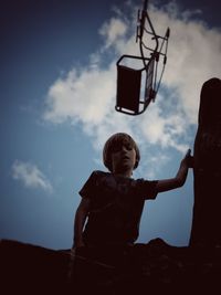 Low angle portrait of boy standing against sky