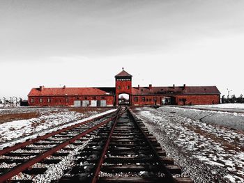 Railroad tracks by building against sky during winter