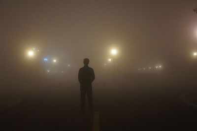 Rear view of silhouette man standing against illuminated lights at night