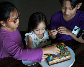 High angle view of cute siblings sitting by cake at home