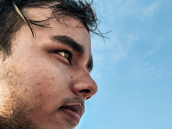 Close-up of young man looking away against sky