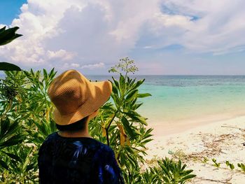 Rear view of woman standing at beach against sky