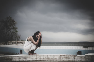 Woman sitting by sea against sky