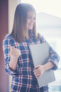 Happy young businesswoman clenching fist while holding laptop in office