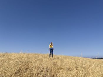 Rear view of woman standing on grass against clear sky
