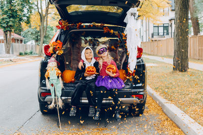 Portrait of smiling sibling sitting in car trunk outdoors