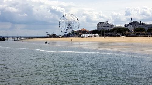 Ferris wheel by sea against sky in city