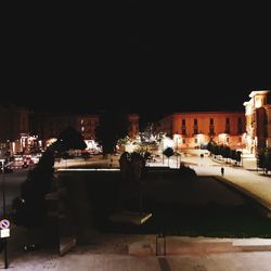 Illuminated street by buildings against sky at night