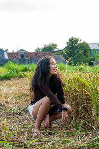 Young woman sitting on rice field against sky.