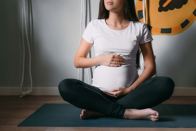 Low section of pregnant woman with hands on stomach sitting at home