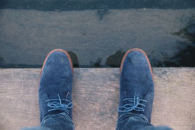 Low section of person standing on wooden plank by the water