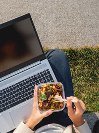 Woman sits on park bench with laptop and  lunch box. bowl with vegetables. healthy nutrition.