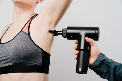 Cropped hand massaging woman with massager against gray background
