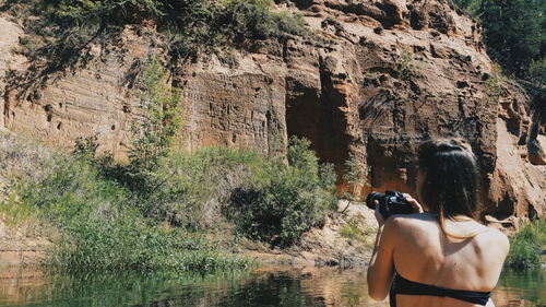 Rear view of woman standing on rock against trees