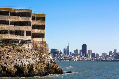 View of city at waterfront against blue sky